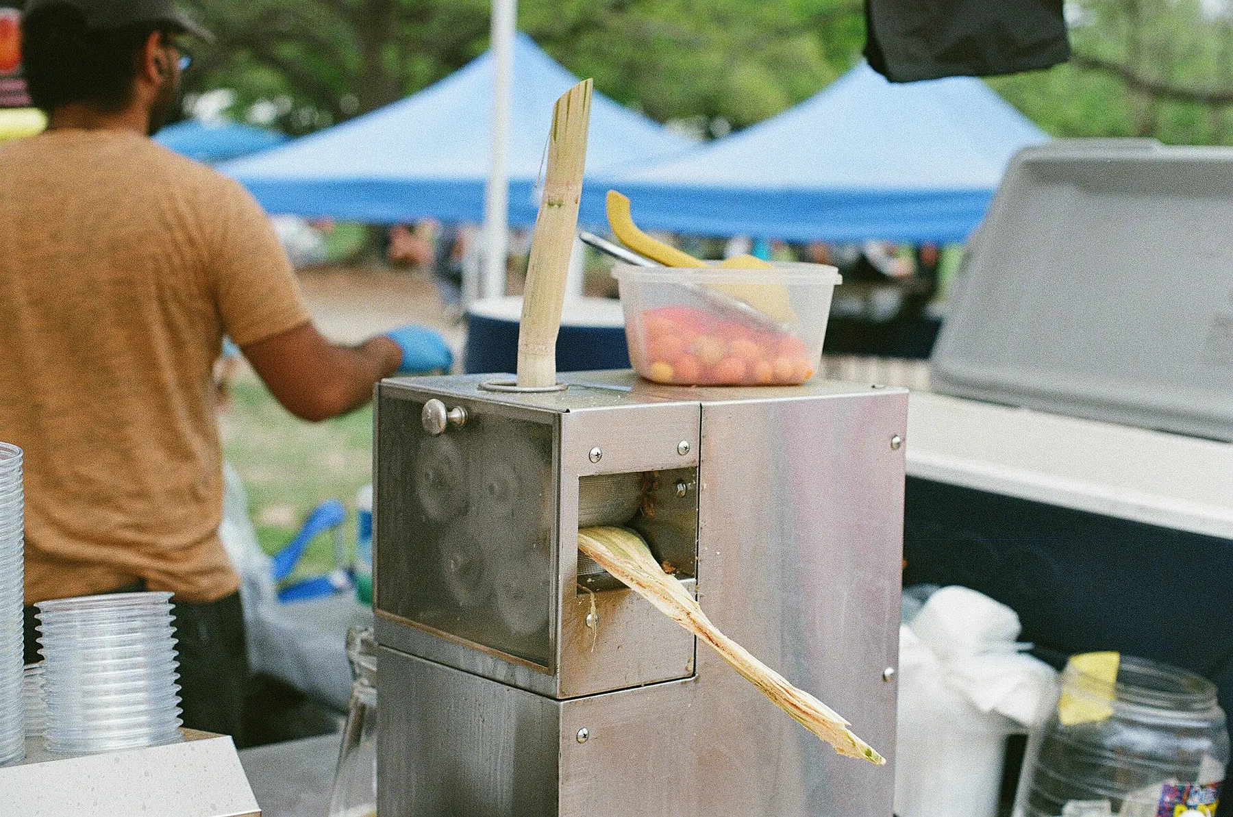 Sugarcane being fed through a stainless steel press at an outdoor stall